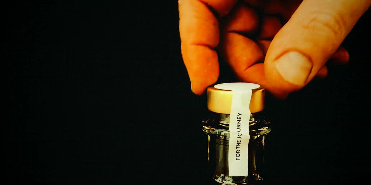 A hand twisting the gold cap off a bottle of True North against a black background