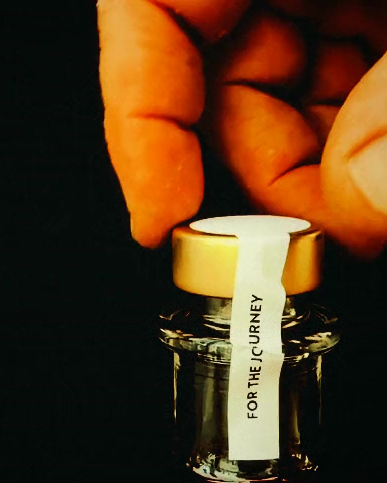 A hand twisting the gold cap off a bottle of True North against a black background